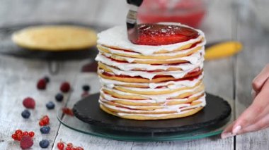Sünger tabakaları lezzetli kek yapma kadın pasta şef eller, dönen kek standı kullanarak krem şanti ve berry reçel.