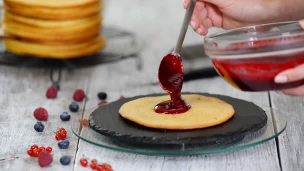 Hände einer Konditorin, die köstlichen Kuchen aus Biskuitschichten, Schlagsahne und Beerenmarmelade mithilfe eines rotierenden Kuchenständers zubereitet. — Stockvideo