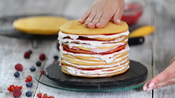 Sünger tabakaları lezzetli kek yapma kadın pasta şef eller, dönen kek standı kullanarak krem şanti ve berry reçel. — Stok video