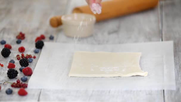 Шеф-повар катит слоеное тесто на пергаментной бумаге. Делать Mille Feuille с ягодами — стоковое видео