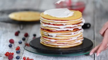 Sünger tabakaları lezzetli kek yapma kadın pasta şef eller, dönen kek standı kullanarak krem şanti ve berry reçel.