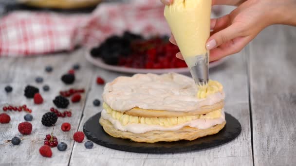 Chef pâtissier utilisant un sac de tuyauterie et un stand de gâteau rotatif pour décorer le gâteau avec du glaçage à la crème debout à la table dans la cuisine à la maison . — Video