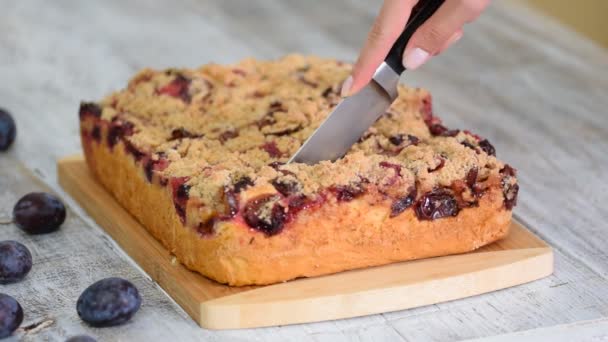 Tarta de ciruela streusel sobre el fondo blanco rústico. Mujer corta pastel — Vídeos de Stock