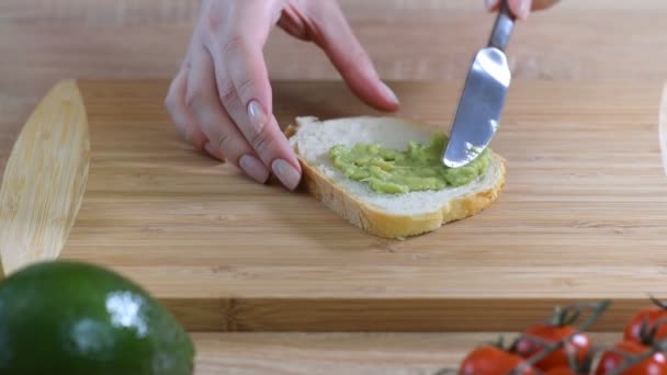 Een vrouw verspreidt aardappelpuree avocado op toast. Gezond ontbijt — Stockvideo