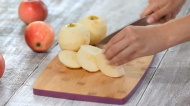 Ev mutfağında ahşap kesme tahtası üzerinde bıçak ile elma dilimleme kadın ellerin closeup.