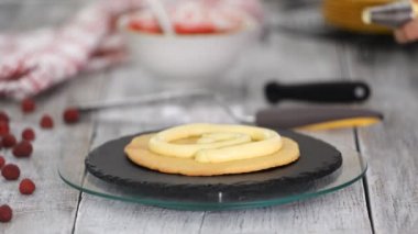 Fırında pasta yapan bir kız. Baker bir pasta boş üzerine krema sıkıyor. Ahşap bir masada beyaz kek.