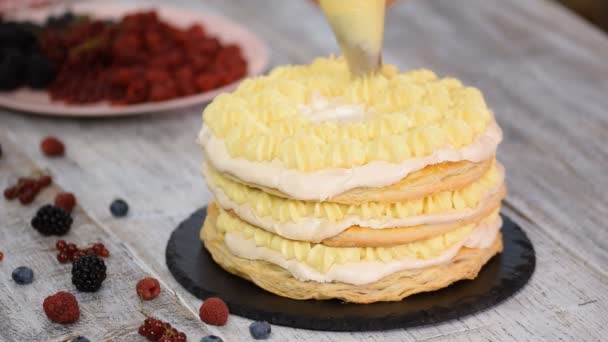 Chef de pastelería femenina usando bolsa de tuberías y soporte de pastel giratorio para decorar la torta con glaseado de crema de pie en la mesa en la cocina casera . — Vídeos de Stock