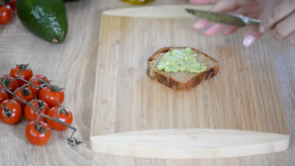 Mujer extendiendo puré de aguacate sobre pan tostado en la mesa, primer plano . — Vídeo de stock