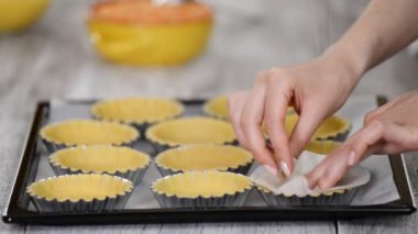Pasta şefi tartlets yapıyor. Konfeksiyoncu küçük levha parşömen ile her tartlet kapağı ve kurutulmuş bezelye ile doldurun. Pişirme süreci.