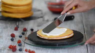 Kremayı katmanlı kekin üzerine süren şekerleme. Böğürtlenli kek yapma süreci.