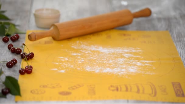 Las manos de las mujeres despliegan la masa en la mesa de la cocina para hacer un pastel con cerezas . — Vídeo de stock