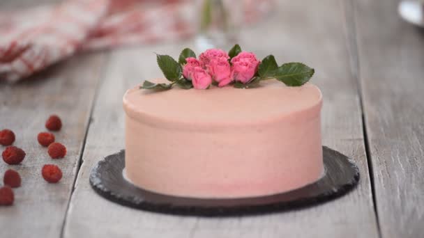 Pastelero pastelero decora cremoso pastel rosa con flores frescas en la mesa — Vídeos de Stock