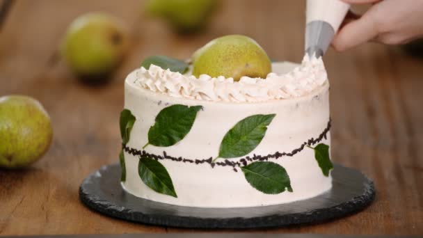 Eine Torte mit Sahne mit Spritzbeutel dekorieren. Konditorin backt Schokoladenkuchen mit Birne. — Stockvideo