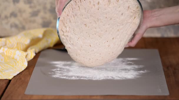 En bagare händer häller bröd deg från en skål på ett köksbord täckt av mjöl. — Stockvideo