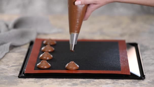 Cooking chocolate profiteroles, female hands squeeze the dough from the bag onto baking sheet. — Stock Video