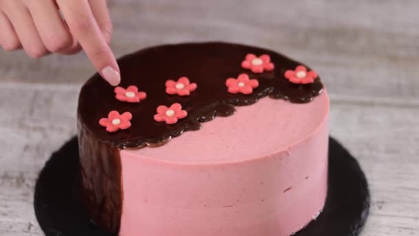 Vrouwelijke handen versieren zelfgemaakte aardbeienmousse cake met suikerbloemen. — Stockvideo