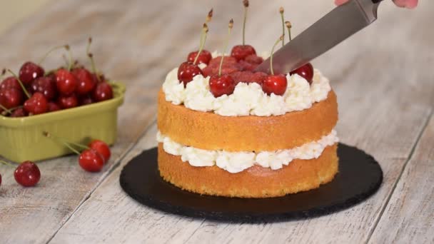 Mujer está cortando el pastel de cereza desnuda con crema de vainilla . — Vídeos de Stock