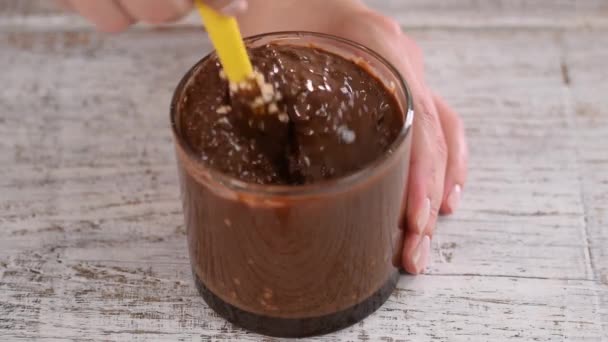 Flüssige dunkle Schokolade mit Nüssen in Schüssel. Weibliche Hand mixt geschmolzene dunkle Schokolade mit Spachtel. — Stockvideo