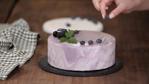 Vrouwen handen versieren een bessen mousse cake met verse bessen op de keukentafel. — Stockvideo