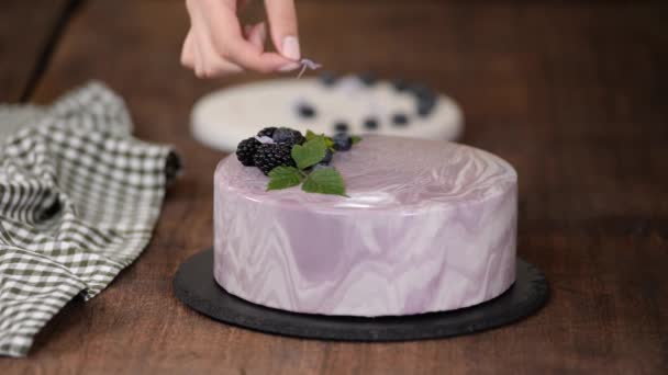 Dłonie kobiet ozdobić mus jagodowy ciasto z kwiatami na stole w kuchni. — Wideo stockowe