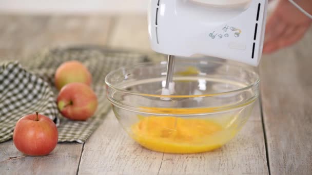 Female hands beating eggs with mixer in the bowl on wooden table. Cooking apple pie in the kitchen — Stock Video