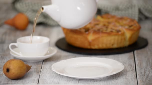 Nierozpoznana osoba wlewa świeżą gorącą herbatę do filiżanki na stole i stawia bułkę na białym talerzu. — Wideo stockowe