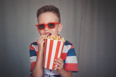 Genç çocuk içinde 3d gözlük sinemada ya da evde bir film izlemek. Küçük çocuk gri arka plan üzerinde patlamış mısır yemek. Ev sineması. Vintage sinema gözlük şirin çocuk. Eğlence kavramının. 