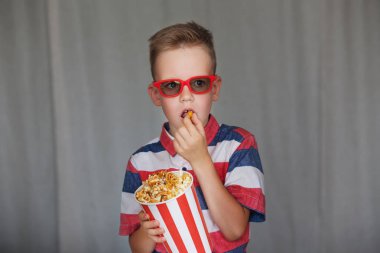Ev sineması. Vintage sinema gözlük şirin çocuk. Eğlence kavramının. Genç çocuk içinde 3d gözlük sinemada ya da evde bir film izlemek. Küçük çocuk gri arka plan üzerinde patlamış mısır yemek. 