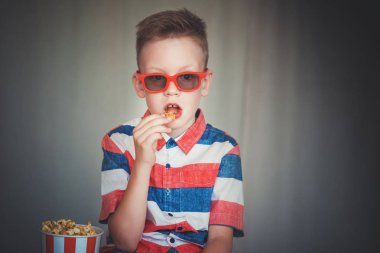 Genç çocuk içinde 3d gözlük sinemada ya da evde bir film izlemek. Küçük çocuk gri arka plan üzerinde patlamış mısır yemek. Ev sineması. Vintage sinema gözlük şirin çocuk. Eğlence kavramının. 