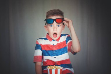 Genç çocuk içinde 3d gözlük sinemada ya da evde bir film izlemek. Küçük çocuk gri arka plan üzerinde patlamış mısır yemek. Ev sineması. Vintage sinema gözlük şirin çocuk. Eğlence kavramının. 