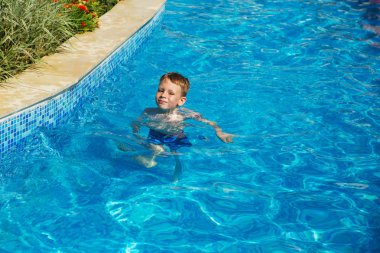 Mavi su havuz tropikal bir çare olarak denizin üzerinde oynayan mutlu çocuk. Yaz tatil kavramı. Sevimli çocuk havuzu suda yüzmek. Sıçramasına ve having fun yüzme havuzunda çocuk