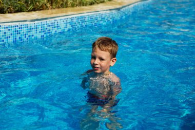 Mavi su havuz tropikal bir çare olarak denizin üzerinde oynayan mutlu çocuk. Yaz tatil kavramı. Sevimli çocuk havuzu suda yüzmek. Sıçramasına ve having fun yüzme havuzunda çocuk