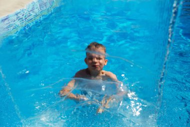 Mavi su havuz tropikal bir çare olarak denizin üzerinde oynayan mutlu çocuk. Yaz tatil kavramı. Sevimli çocuk havuzu suda yüzmek. Sıçramasına ve having fun yüzme havuzunda çocuk