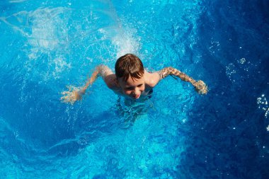 Mavi su havuz tropikal bir çare olarak denizin üzerinde oynayan mutlu çocuk. Yaz tatil kavramı. Sevimli çocuk havuzu suda yüzmek. Sıçramasına ve having fun yüzme havuzunda çocuk