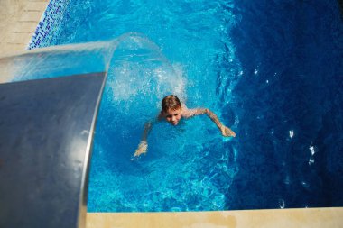 Mavi su havuz tropikal bir çare olarak denizin üzerinde oynayan mutlu çocuk. Yaz tatil kavramı. Sevimli çocuk havuzu suda yüzmek. Sıçramasına ve having fun yüzme havuzunda çocuk