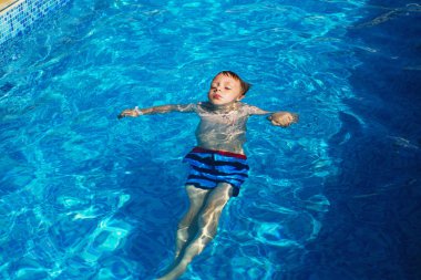 Mavi su havuz tropikal bir çare olarak denizin üzerinde oynayan mutlu çocuk. Yaz tatil kavramı. Sevimli çocuk havuzu suda yüzmek. Sıçramasına ve having fun yüzme havuzunda çocuk