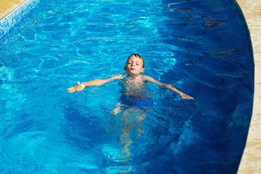 Mavi su havuz tropikal bir çare olarak denizin üzerinde oynayan mutlu çocuk. Yaz tatil kavramı. Sevimli çocuk havuzu suda yüzmek. Sıçramasına ve having fun yüzme havuzunda çocuk