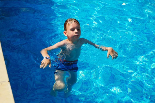 幸せな子供の海でトロピカル リゾートのスイミング プールのブルーの水で遊ぶ 夏の休暇の概念 プールの水で泳いでいるかわいい少年です 水しぶきとスイミング プールで楽しい子 — ストック写真