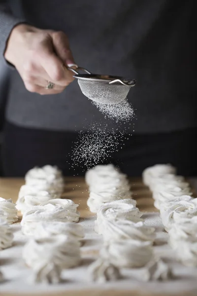 The process of making marshmallow. Close up hands of the chef with metal sieve sprinkling zephyr with Powdered sugar at pastry shop kitchen. confectioner sprinkles sugar powder confectionery