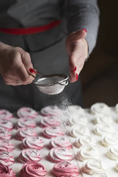 The process of making marshmallow. Close up hands of the chef with metal sieve sprinkling zephyr with Powdered sugar at pastry shop kitchen. confectioner sprinkles sugar powder confectionery