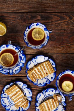 Tatil hala hayat. Lezzetli kek parçaları ve grunge ahşap arka plan üzerinde limonlu çay bardak ile plakalar. Atış düz yatıyordu öğleden sonra kahve molası masa üstü. Delftware beyaz ve mavi çay seti çarpıcı 