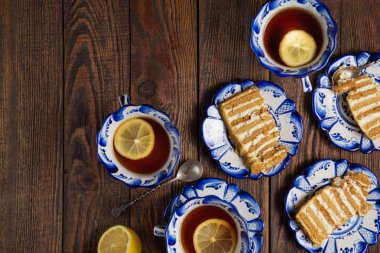 Tatil hala hayat. Lezzetli kek parçaları ve grunge ahşap arka plan üzerinde limonlu çay bardak ile plakalar. Atış düz yatıyordu öğleden sonra kahve molası masa üstü. Delftware beyaz ve mavi çay seti çarpıcı 