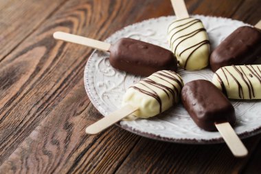 Sütlü çikolata çubuklu dondurmayı sopa üzerinde. Dondurma çubuklu dondurmayı plaka ahşap arka plan üzerinde beyaz ve koyu çikolata kaplı. Metin için yer. Çikolatalı dondurma çubukları, fındık. Dondurma tatlı