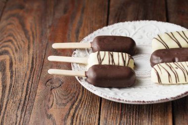 Sütlü çikolata çubuklu dondurmayı sopa üzerinde. Dondurma çubuklu dondurmayı plaka ahşap arka plan üzerinde beyaz ve koyu çikolata kaplı. Metin için yer. Çikolatalı dondurma çubukları, fındık. Dondurma tatlı