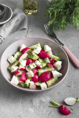 Gri üzerinde bir kasede turp, salatalık, kivi, peynir ve dereotu salatası 