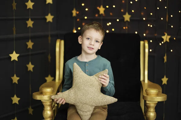 En vacker liten pojke sitter i en stol kramar en stjärnformad piller — Stockfoto