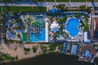 Su parkının en üst manzarası, havuzlu ve su kaydırağlı. Baraj gölünün kıyısında bir yerde. Çok renkli su kayakları, büyük mavi bir havuz ve dinlenen insanlar..