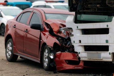 Bir araba ve kamyon arasındaki kafa kafaya çarpışmadan sonra. Kırmızı araba ağır hasar görmüş: kaput parçalanmış, far ve tampon kırılmış ve parçalar yola saçılmış..