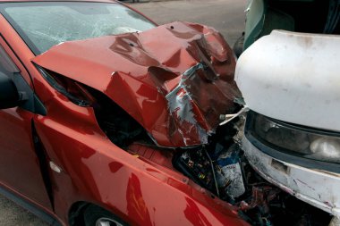 Bir araba ve kamyon arasındaki kafa kafaya çarpışmadan sonra. Kırmızı araba ağır hasar görmüş: kaput parçalanmış, far ve tampon kırılmış ve parçalar yola saçılmış..
