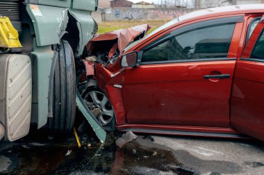 Bir araba ve kamyon arasındaki kafa kafaya çarpışmadan sonra. Kırmızı araba ağır hasar görmüş: kaput parçalanmış, far ve tampon kırılmış ve parçalar yola saçılmış..